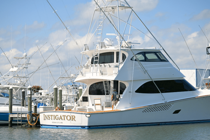 Large white yacht named 'Instigator' docked in marina, surrounded by other boats.