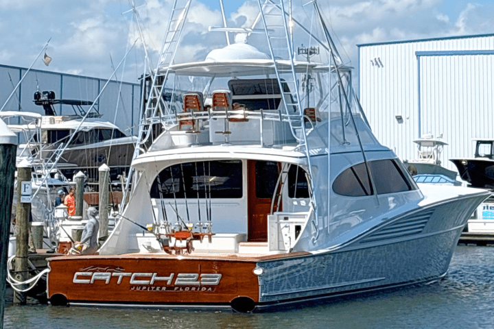 Large fishing boat named 'CATCH 23' docked at marina with rods and blue sky background.