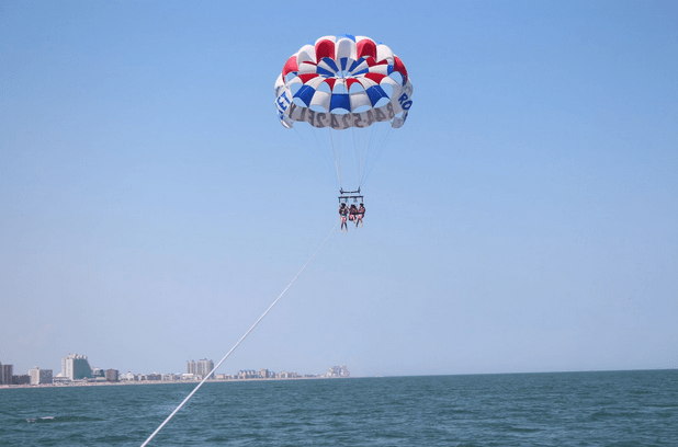 Two people parasailing over the ocean with a colorful parachute near the coast.