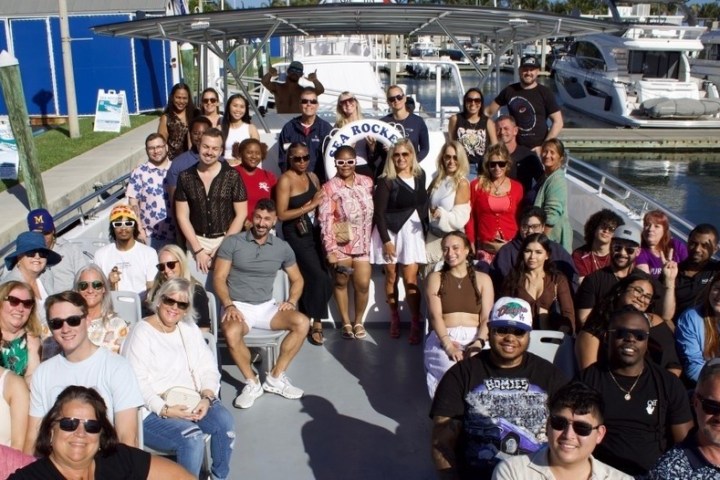Group of people sitting on a boat at a marina, posing for a photo on a sunny day.