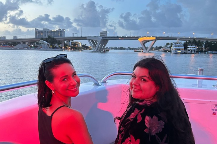Two people sitting on a boat with a bridge and water in the background at sunset.