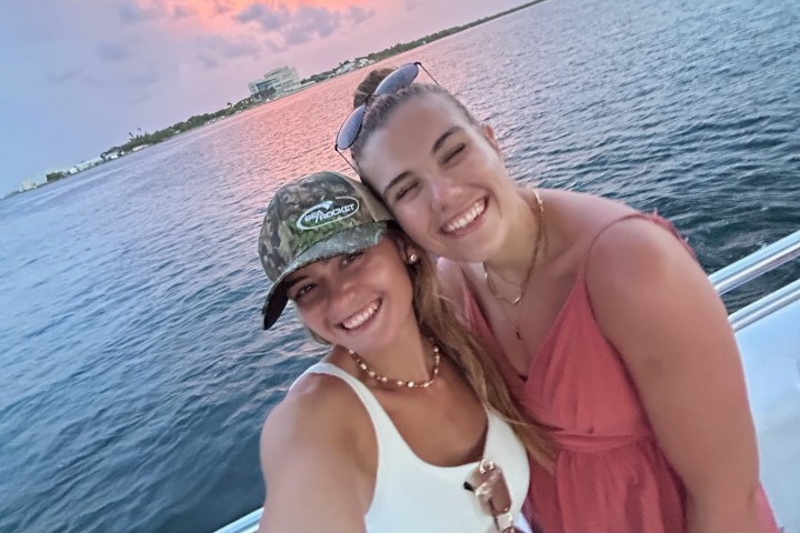 Two people taking a selfie on a boat with a sunset over the water in the background.