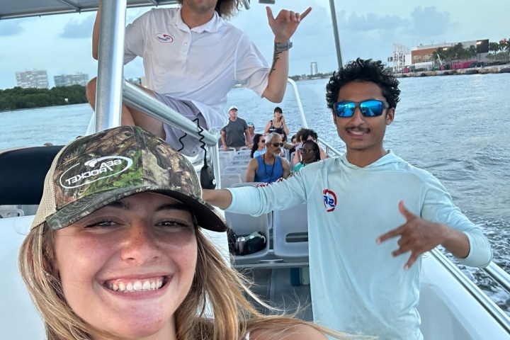 Smiling people on a boat, posing with hand gestures, under a clear sky.