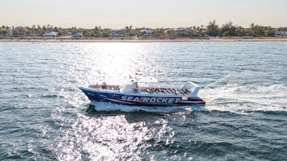 A speedboat named 'Sea Rocket' cruising on a sunny ocean near a coastal town.