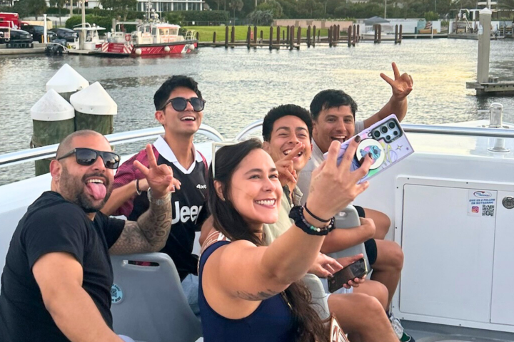 Group of friends taking a selfie on a boat, smiling and making peace signs.
