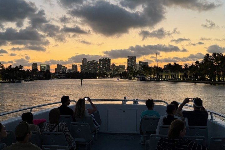 Silhouetted people on a boat at sunset with a city skyline in the background.