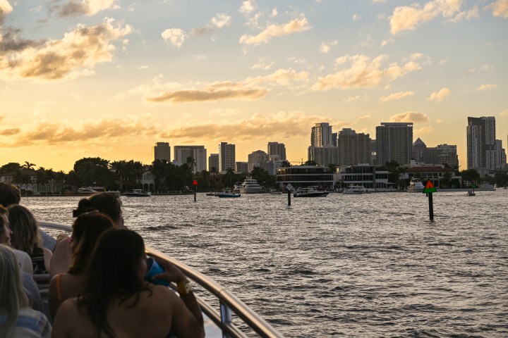 People on a boat with a city skyline and sunset in the background.