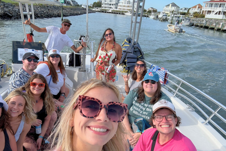Group of people smiling on a boat with houses and water in the background.