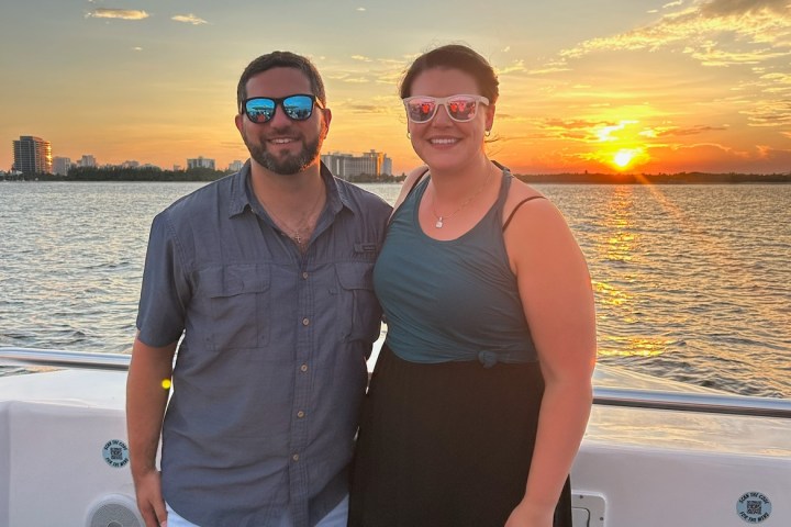 Two people on a boat at sunset with city skyline in the background.