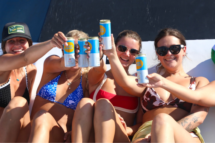 Group of people in swimwear toasting with canned drinks on a boat.