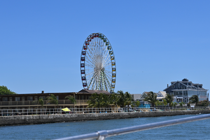 Ferris wheel and buildings by waterfront under clear blue sky.