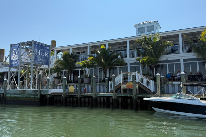 Waterfront building with palm trees, large sign, and docked boat in sunny weather.