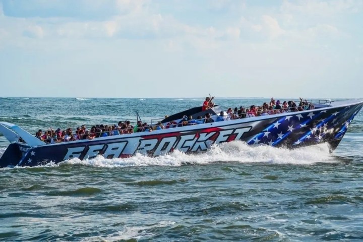 Large speedboat named 'Sea Rocket' with passengers, decorated in stars, cruising on the ocean.