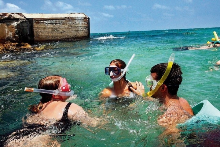 Group of snorkelers swimming near a concrete structure in clear ocean water.