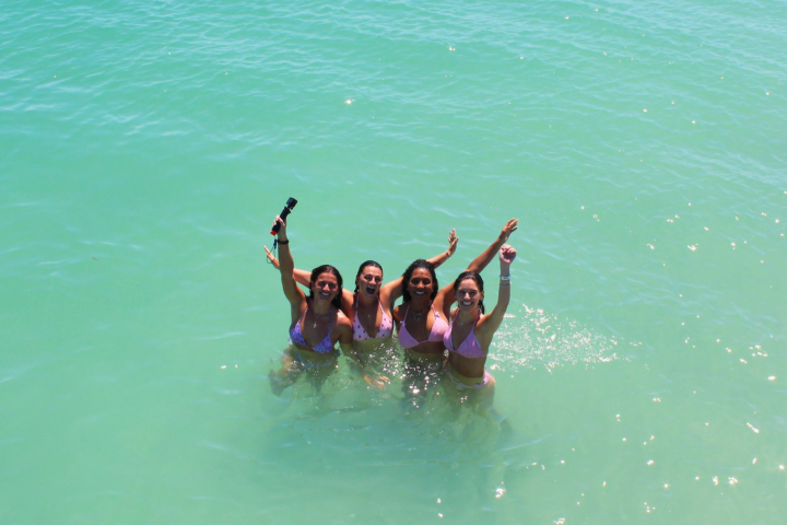 Four people in swimsuits enjoying the ocean, raising arms with smiles.