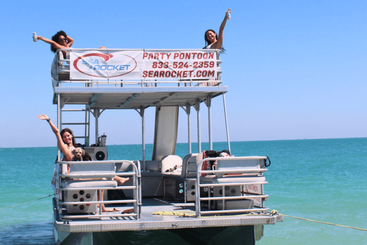 Party pontoon boat with people waving on a sunny day at sea.