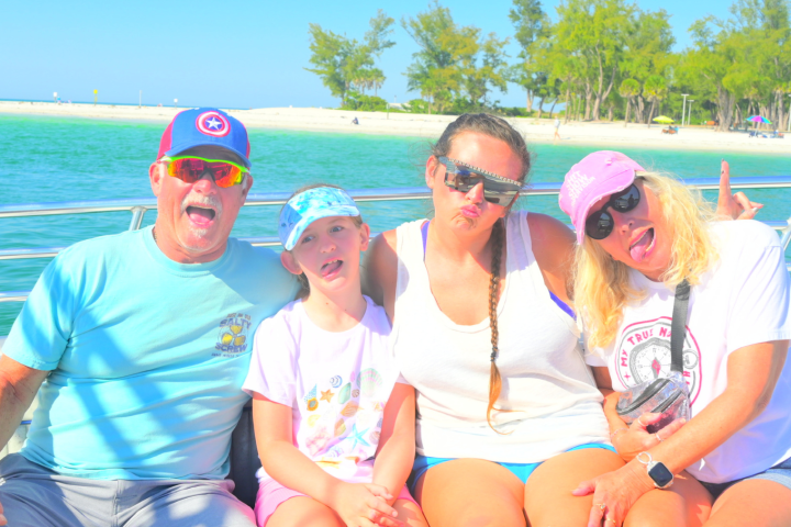 A family enjoying a fun moment together on a private boat cruise near Bradenton Beach with clear turquoise water in the background.
