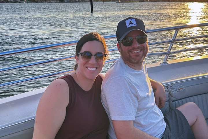 Two people smiling on a boat at sunset with water in the background.