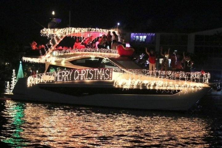 Boat decorated with Christmas lights and 'Merry Christmas' sign at night.