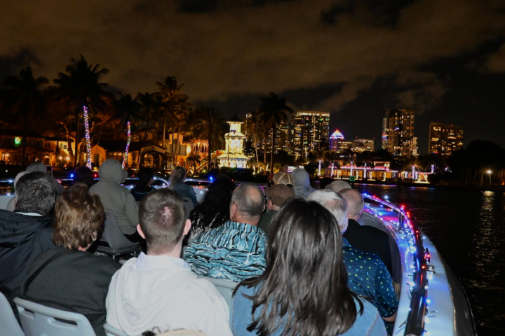People on a boat at night with a city skyline and palm trees in the background.