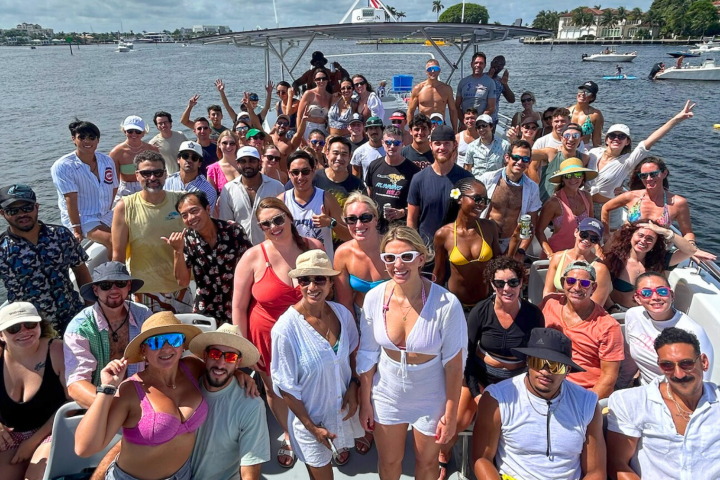 Large group of people on a boat, smiling and posing, with water and other boats in the background.