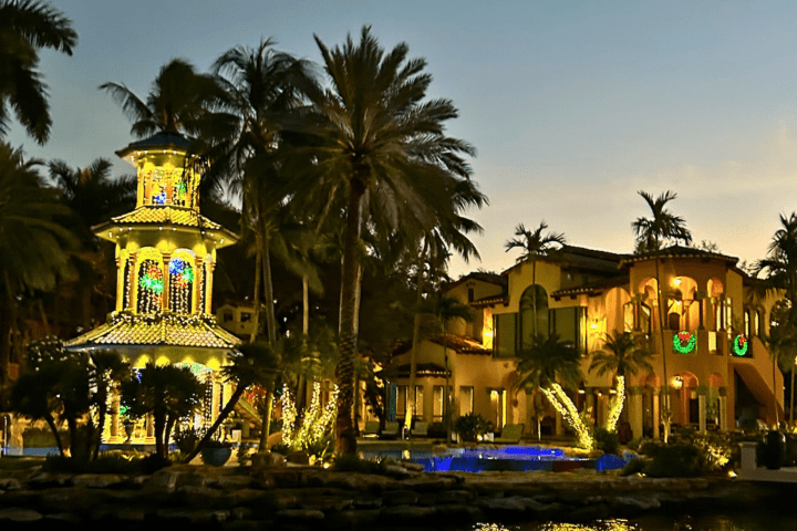 Illuminated gazebo and house with palm trees at dusk.
