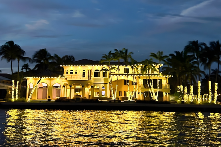Large house with festive lights reflected in water at dusk.