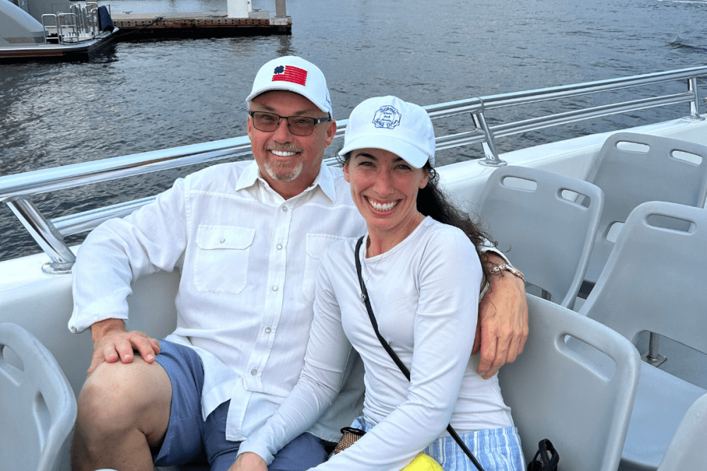 Two people in hats sitting on a boat with a body of water in the background.