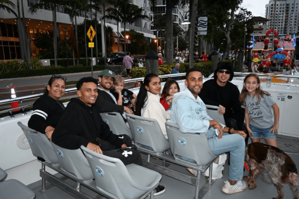 Group of people smiling on a boat with city buildings and palm trees in the background.