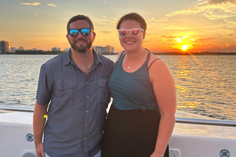 Two people on a boat at sunset with city skyline in the background.