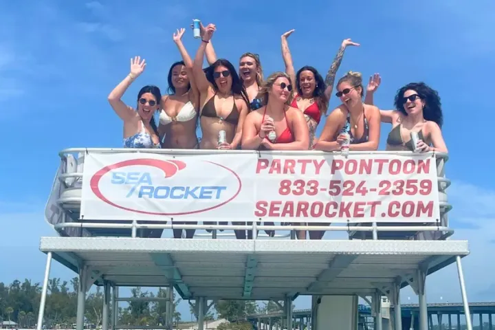 Group of women in swimsuits on boat with 'Sea Rocket' sign, clear sky.