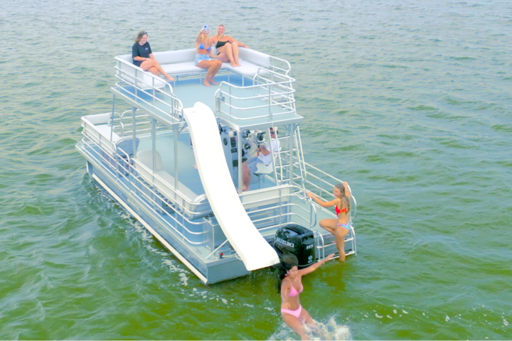 People relaxing on a pontoon boat with a slide in the water.