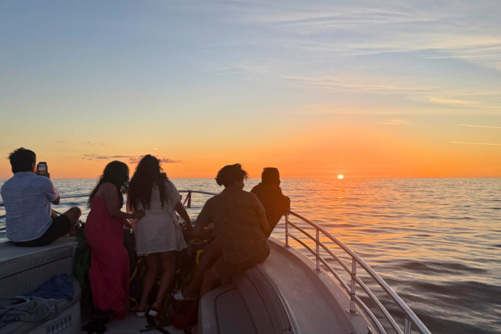 Group of people on a boat watching the sunset over the ocean.
