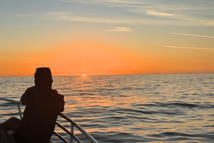 Silhouette of a person on a boat at sunset over calm ocean waves.