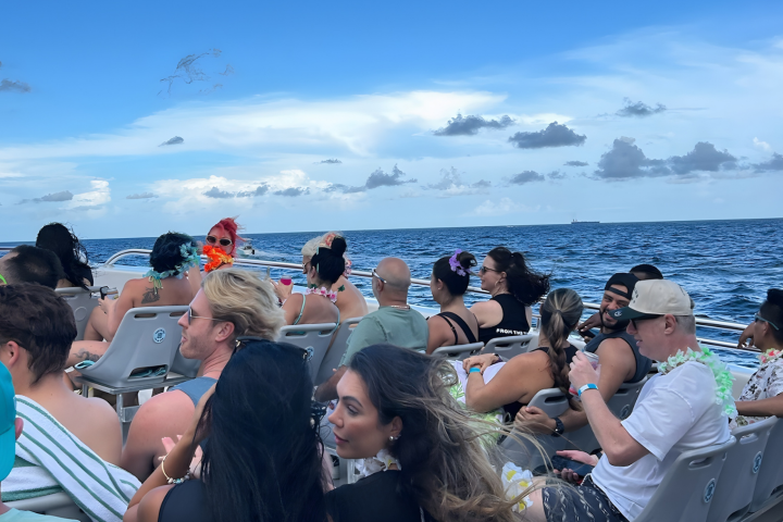 Group of people sitting on a boat, looking at the ocean under a partly cloudy sky.