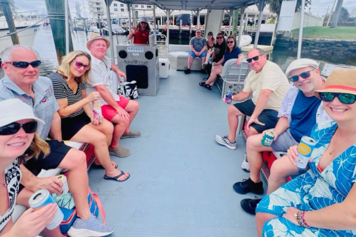 Group of people seated on a boat, holding drinks, smiling at the camera.