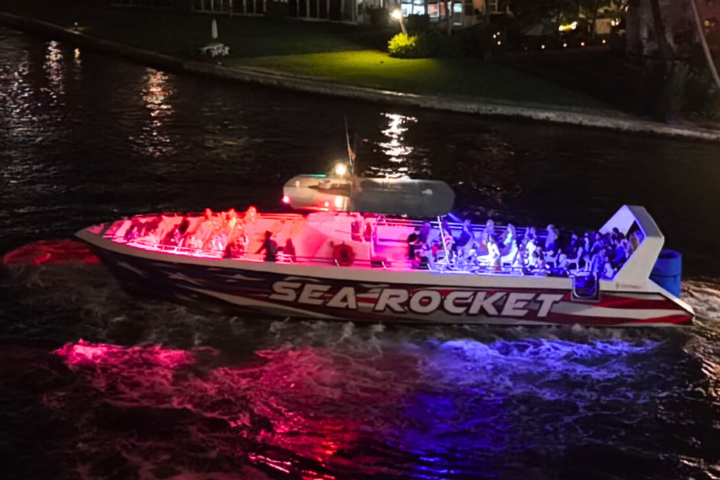 Illuminated tour boat named Sea Rocket on water at night with red and blue lights.