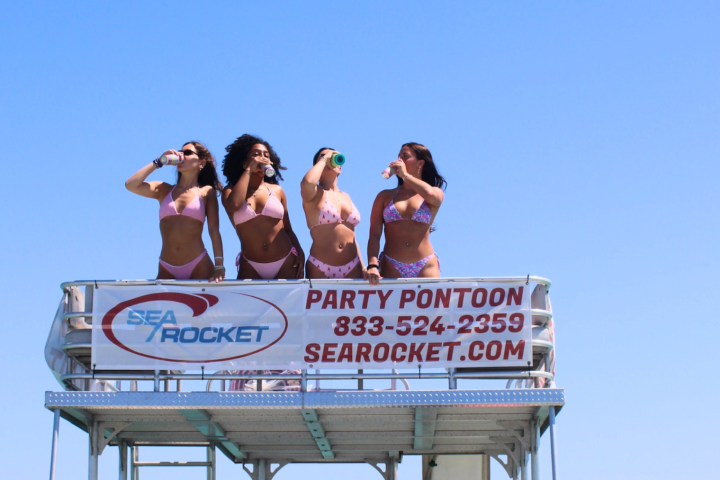 Four people in swimwear on a pontoon, clear sky in background.