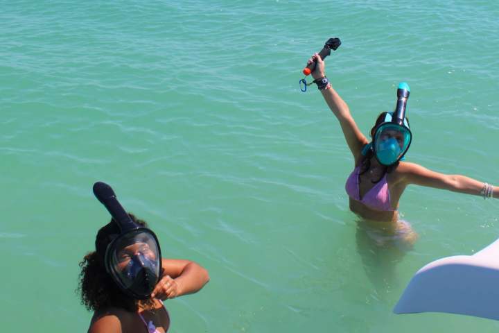 Two people snorkeling in clear water, one with arms raised holding a camera.