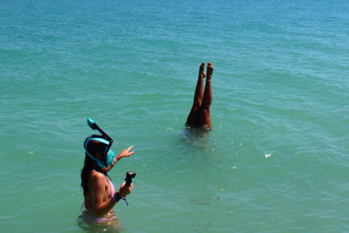 Person snorkeling, another does a handstand in the ocean.