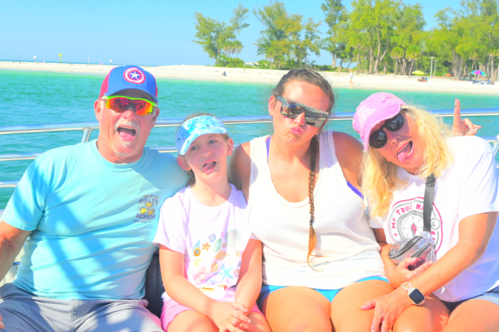 Four people smiling and posing on a boat with a beach in the background.