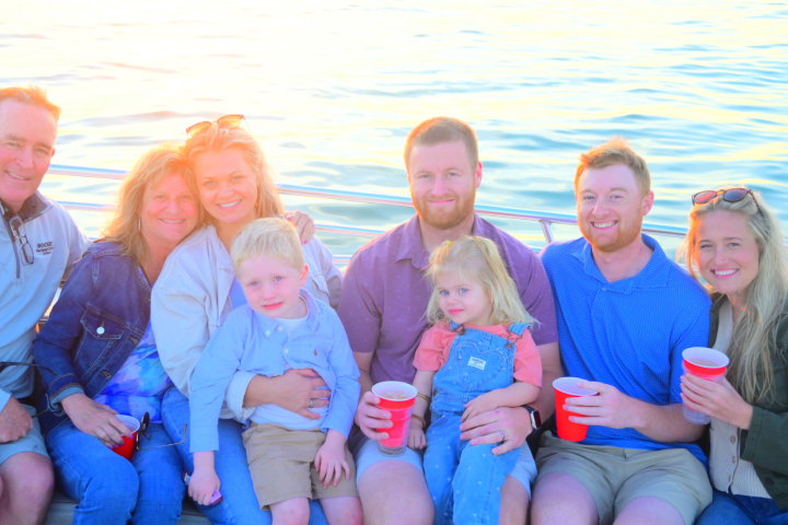 Group of seven adults and two children smiling on a boat holding red cups.