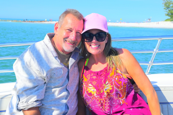 Smiling couple on a boat with ocean and beach in background.