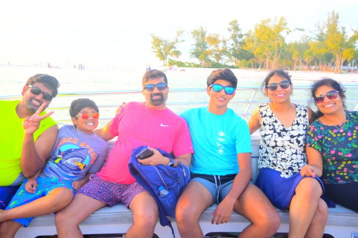 Group of six people smiling on a boat, with trees and water in the background.
