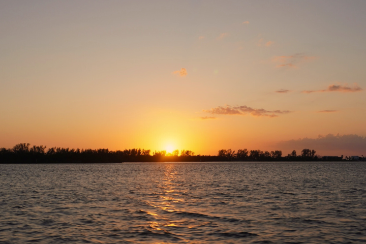 Sunset over a calm lake with trees silhouetted on the horizon, orange sky above.