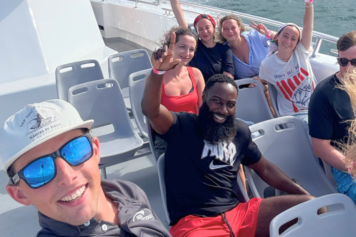 Group of people smiling and waving on a boat outdoors.