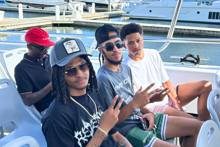 Four men sitting on a boat with a marina in the background.