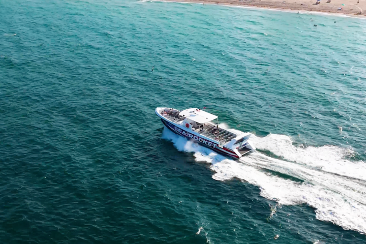 A speedboat cruising on teal water near a sandy shore.