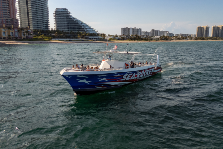 Speedboat with 'Sea Rocket' on side cruising near city shoreline.