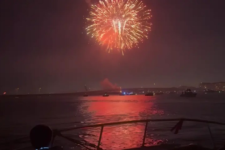 Bright fireworks illuminating the night sky over a calm body of water.